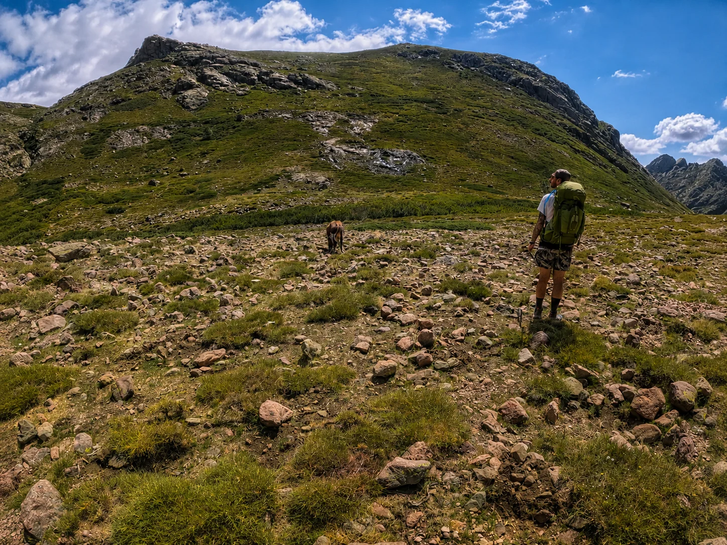 Randonneur avec sac vert face à une montagne corse sur le GR20